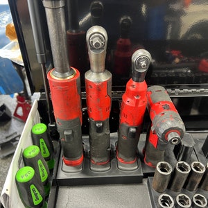 May include: Four red and black cordless impact wrenches are displayed in a black holder. The wrenches are arranged in order of size, with the largest wrench on the left and the smallest wrench on the right. The wrenches are all in a new condition and have not been used.