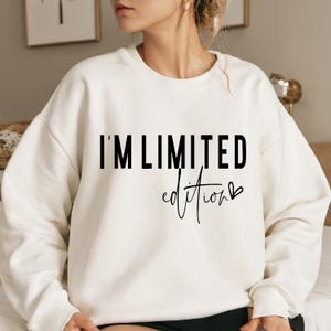 May include: Cream-colored sweatshirt with the text "I'M LIMITED edition" in black block letters and cursive script. The sweatshirt has a crew neck and long sleeves. The design is centered on the front of the garment.