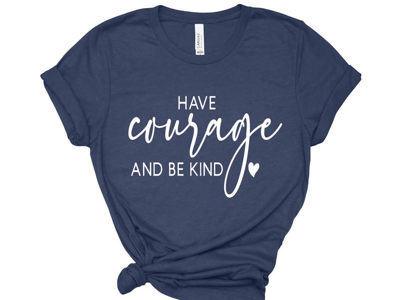 May include: Navy blue t-shirt with the words "HAVE courage AND BE KIND" in white script. A small white heart is next to the word "KIND". The shirt is folded at the bottom.