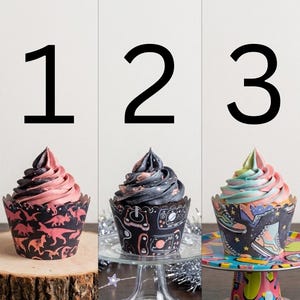 May include: Three cupcakes with colorful frosting and decorative wrappers. The first cupcake has pink and black frosting and a dinosaur-themed wrapper. The second has black and pink frosting with a space-themed wrapper. The third has pastel frosting and a shoe-themed wrapper.