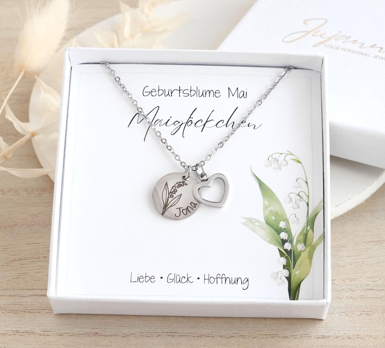 May include: A silver necklace with a lily of the valley charm and a heart charm. The charm has the name "Jona" engraved on it. The necklace comes in a white box with a card that says "Geburtsblume Mai Maigl&ouml;ckchen Liebe Gl&uuml;ck Hoffnung".