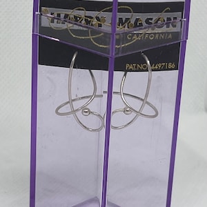 May include: A pair of silver-toned hoop earrings with a curved, looped design and a small spherical accent, housed in a tall, transparent purple plastic display case. The packaging features the text Harry Mason California and PAT. NO 4497186.