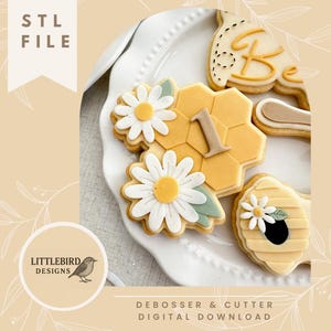 Peut inclure: Assortiment de biscuits au sucre décorés sur une assiette blanche. Les biscuits présentent des motifs de marguerites et de nids d'abeilles, avec le chiffre "1" et le mot "Be". L'image comprend le texte "STL FILE" et "DEBOSSER & CUTTER DIGITAL DOWNLOAD". Le logo Littlebird Designs est également visible.
