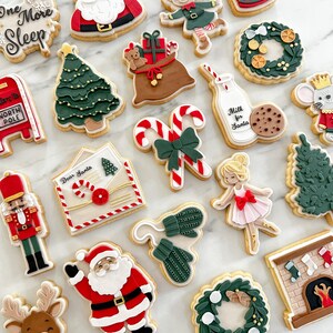 May include: A collection of Christmas-themed cookies, including Santa Claus, elves, reindeer, Christmas trees, wreaths, and a mailbox. Some cookies have text that reads "One More Sleep" and "Milk for Santa". The cookies are decorated with colorful icing.