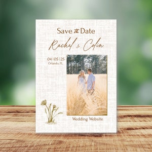 Pode incluir: Cartão Save the Date com textura de linho rústico. O cartão apresenta uma foto de um casal em um campo, com o texto "Save the Date Rachel & Colin 04 05 | 25 Orlando, FL Wedding Website".