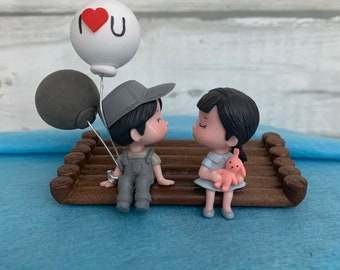 Figura de pareja besándose: niño de resina con globos, niña con conejito