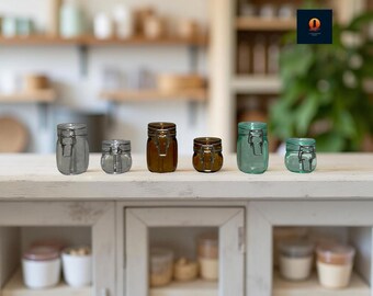 May include: A collection of six glass jars with metal clasps in varying sizes and colors, including gray, clear, brown, and teal. The jars are arranged on a white surface, with a blurred kitchen background.