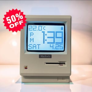 Peut inclure: Une horloge de bureau numérique beige en forme d'ordinateur vintage avec un écran affichant 22.0°C, 1:39 PM, SAT et 4.25. L'avant présente une étiquette Maclock, un petit logo pomme arc-en-ciel et une fente. Un graphique rouge indique 50% OFF.