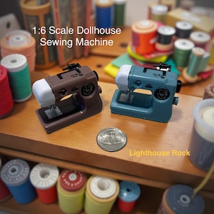 May include: Two miniature sewing machines, one brown and one teal, with white accents, are displayed on a wooden surface. The text "1:6 Scale Dollhouse Sewing Machine" is visible. A coin and spools of thread are also present.