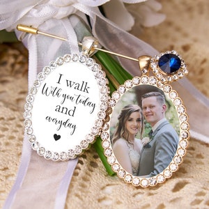 Può includere: Due spille per bouquet da sposa di forma ovale. Una spilla presenta una foto di una sposa e uno sposo, e l'altra spilla ha il testo "Cammino con te oggi e ogni giorno" con un piccolo cuore.