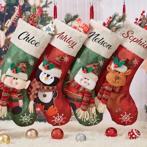 May include: Four personalised Christmas stockings featuring different characters. The stockings are red and green with white snowflakes and are decorated with an elf, penguin, snowman, and reindeer. The stockings are personalised with the names Chloe, Ashley, Nelson, and Sophia.