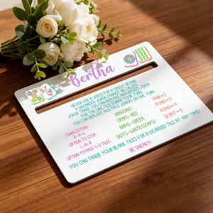 May include: A white Mahjong tile holder with a slot, featuring game rules and the name "Bertha" in purple script. Colorful Mahjong tile illustrations and a bouquet of white roses are also visible.