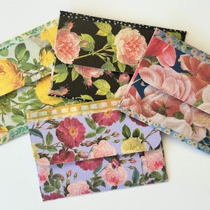 May include: Four rectangular envelopes featuring floral patterns. One has yellow roses on a light green background, one has pink roses on a black background, one has pink roses on a blue background, and one has mixed roses on a light purple background.
