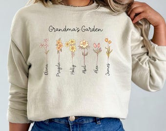 May include: Beige sweatshirt with the text "Grandma's Garden" and floral illustrations. Each flower has a name: Olivia, Fragile, Holly, Abel, Alex, and James. The sweatshirt is a neutral color.