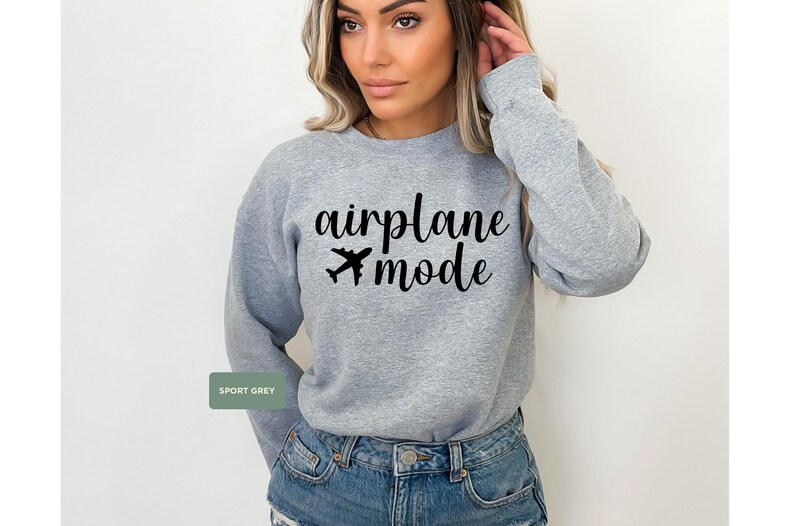 May include: Sport grey sweatshirt with the words "airplane mode" in black script and a small airplane graphic. The sweatshirt is a crew neck style and is made of a soft material. The model is wearing blue denim shorts.