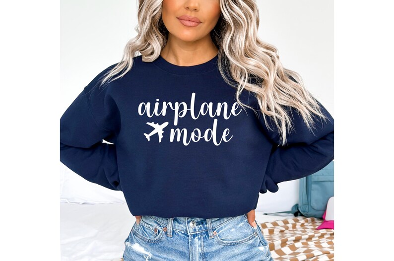 May include: Navy blue sweatshirt with the words "airplane mode" and a white airplane graphic. The text is in a cursive font. The sweatshirt is paired with blue jeans.