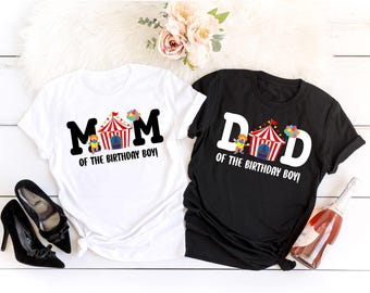 May include: Two t-shirts, one white and one black, with circus-themed graphics. The white shirt says "MOM of the BIRTHDAY BOY!" and the black shirt says "DAD of the BIRTHDAY BOY!" Both shirts have a circus tent and balloon design.