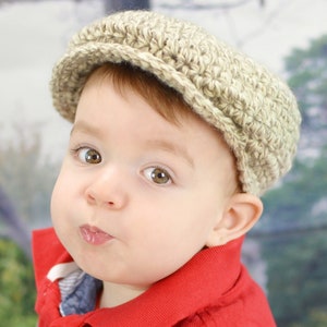 May include: A baby wearing a beige crocheted newsboy cap and a red polo shirt.