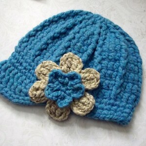 Puede incluir: Un gorro de punto azul con un adorno de flor beige.