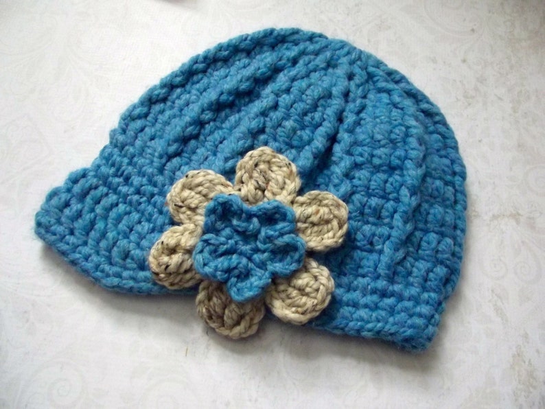 Puede incluir: Un gorro de punto azul con un adorno de flor beige.