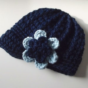 Puede incluir: Un gorro de punto azul marino con una flor de punto azul claro.