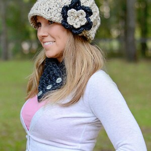 May include: A woman wearing a beige crocheted hat with a black flower accent and a black crocheted scarf with buttons.