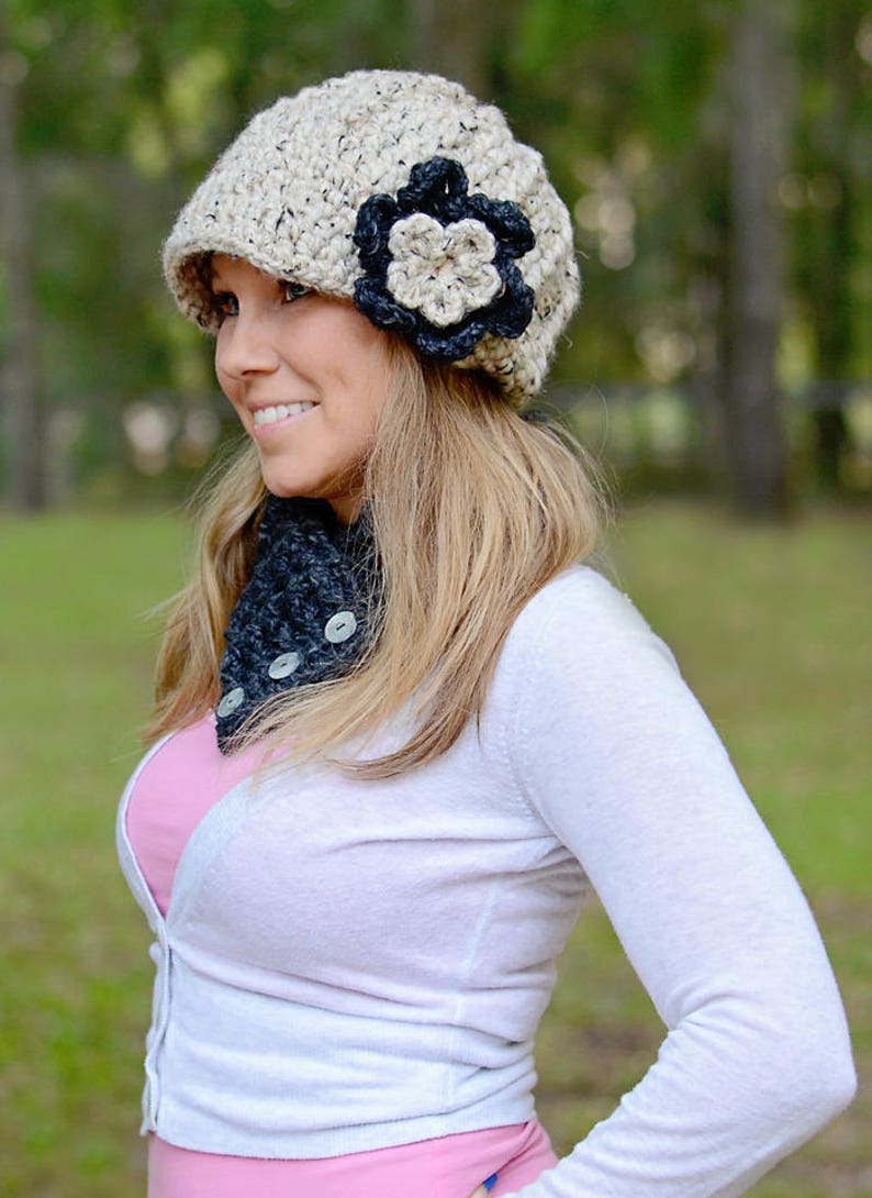 May include: A woman wearing a beige crocheted hat with a black flower accent and a black crocheted scarf with buttons.