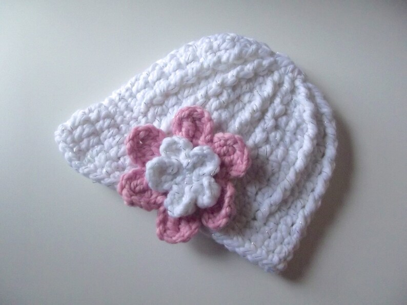 Puede incluir: Sombrero blanco de ganchillo con un adorno de flor rosa y blanca.