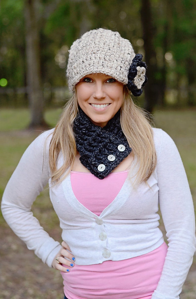 Puede incluir: Una mujer con un c&aacute;rdigan blanco, un top rosa, un cuello de lana negro y blanco con botones y un gorro de punto beige con una flor negra.