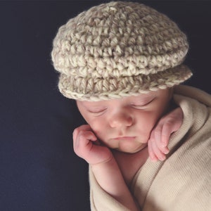 May include: A sleeping baby wearing a beige crocheted hat and wrapped in a beige blanket.