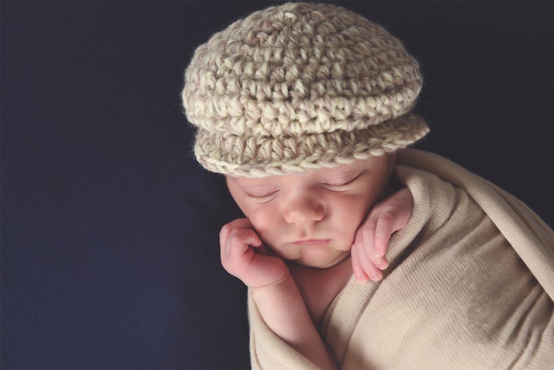 May include: A sleeping baby wearing a beige crocheted hat and wrapped in a beige blanket.