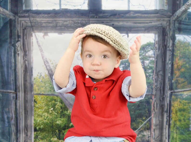 May include: A young child wearing a red polo shirt and a beige knitted cap. The child is looking at the camera with a serious expression.