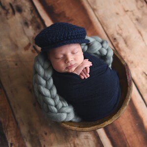 May include: A newborn baby wearing a blue knitted cap is sleeping in a woven basket. The baby is wrapped in a blue blanket and is lying on a light blue braided rope.