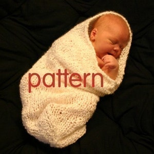 May include: A white knitted baby swaddle with a pattern. The swaddle is wrapped around a sleeping baby.