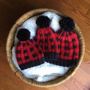 May include: Three knitted hats with black and red buffalo plaid patterns and black pom-poms.