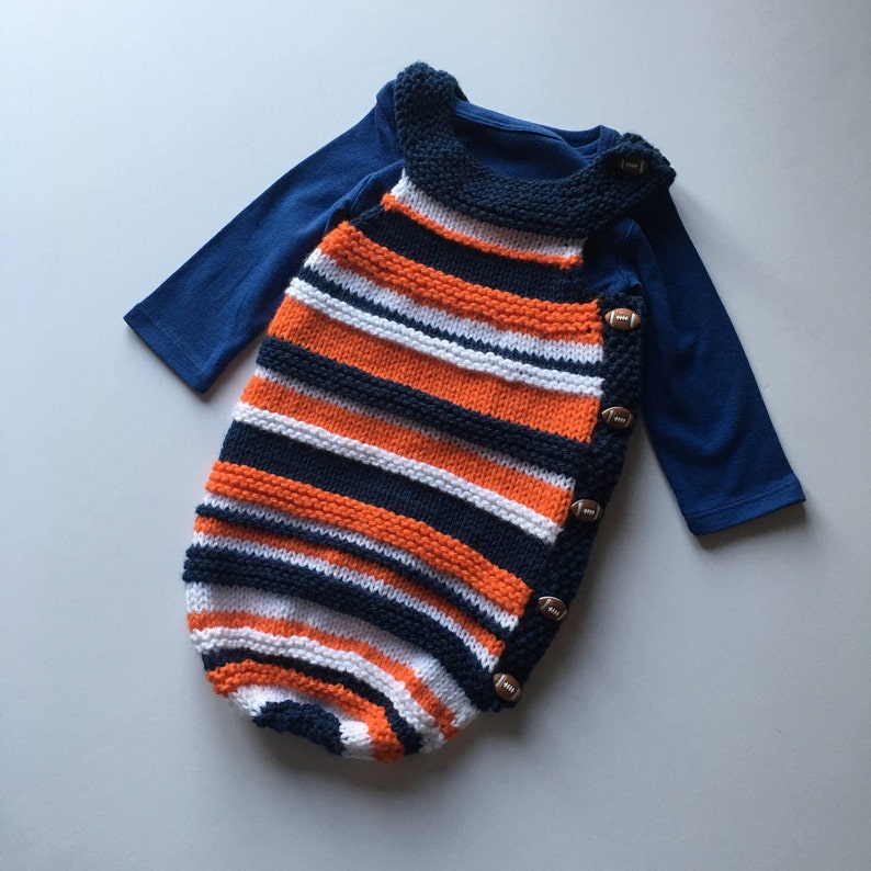 May include: A knitted baby sleeper with orange, white, and navy blue stripes. The sleeper has a football-shaped button closure on the side.