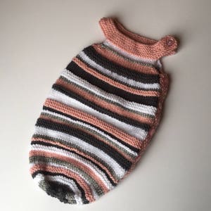 May include: A pink, white, gray, and black striped knitted baby sleeping bag with a button closure.