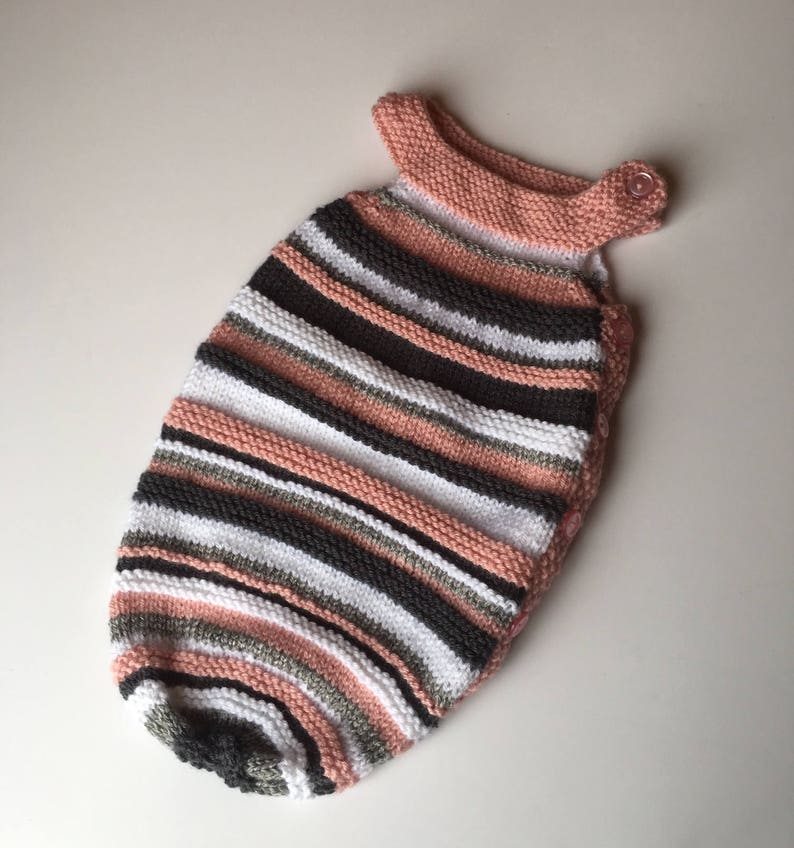 May include: A pink, white, gray, and black striped knitted baby sleeping bag with a button closure.