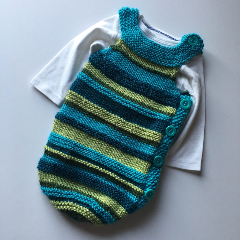 May include: A striped knitted baby sleeping bag in teal and green with turquoise buttons.