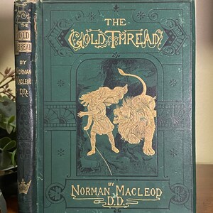 Peut inclure: Un livre vert avec des lettres dorées intitulé "The Gold Thread" par Norman Macleod D.D. La couverture présente une illustration d'une fille menant un lion avec une corde dorée.