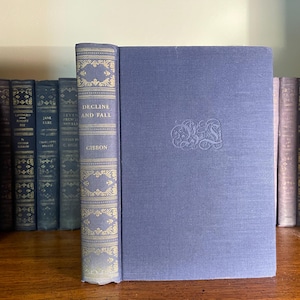 May include: A blue hardcover book with the title "Decline and Fall" by Gibbon on the spine. The book is on a bookshelf with other books.