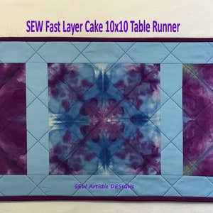 May include: A blue and purple tie-dye table runner with a quilted design. The runner is 10 inches by 10 inches and has three squares with different tie-dye patterns. The text "SEW Fast Layer Cake 10x10 Table Runner" is at the top of the image. The text "SEW Artistic Designs" is at the bottom of the image.