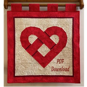 May include: A red and cream-coloured quilted wall hanging with a heart design. The heart is made of interwoven red fabric. The text "PDF Download" is visible. Finished size is 71 cm x 71 cm.