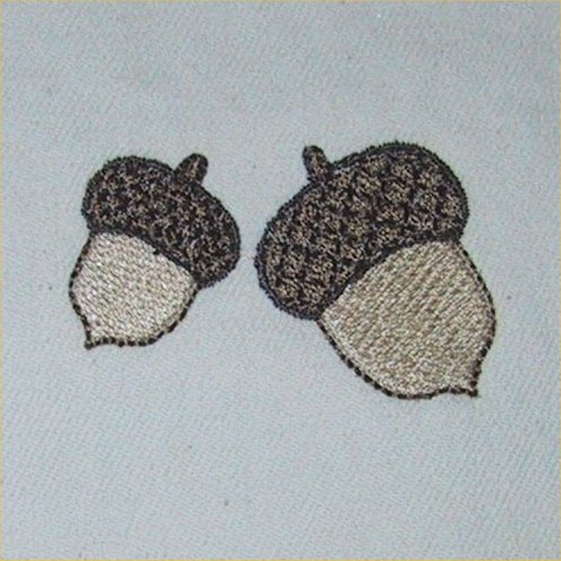 May include: Two embroidered acorns with brown caps and beige bottoms. The acorns are stitched with a detailed pattern.