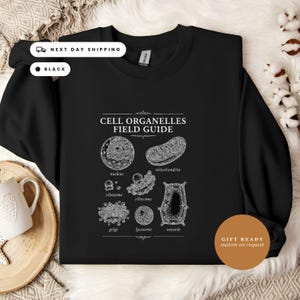 May include: A black long-sleeve sweatshirt featuring a white graphic print titled Cell Organelles Field Guide. The design displays detailed scientific illustrations of a nucleus, mitochondria, ribosomes, golgi, lysosome, and vacuole with labels.