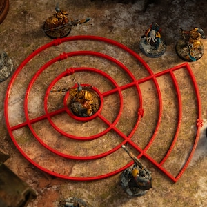 May include: A red plastic template with concentric circles and lines for use in tabletop games. The template is on a brown surface with several miniature figures painted in gold and green.