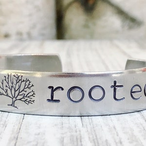 May include: A silver bracelet with the words "deeply rooted" and a small tree design engraved on it.