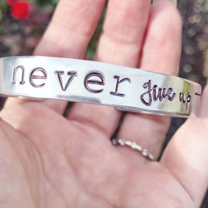 May include: Silver bracelet with the words "never give up" engraved on it.