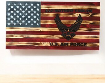 May include: A wooden American flag with a burnt wood finish. The flag features the Air Force emblem and the text "A1C Mathew Yarlon" and "U.S. Air Force".