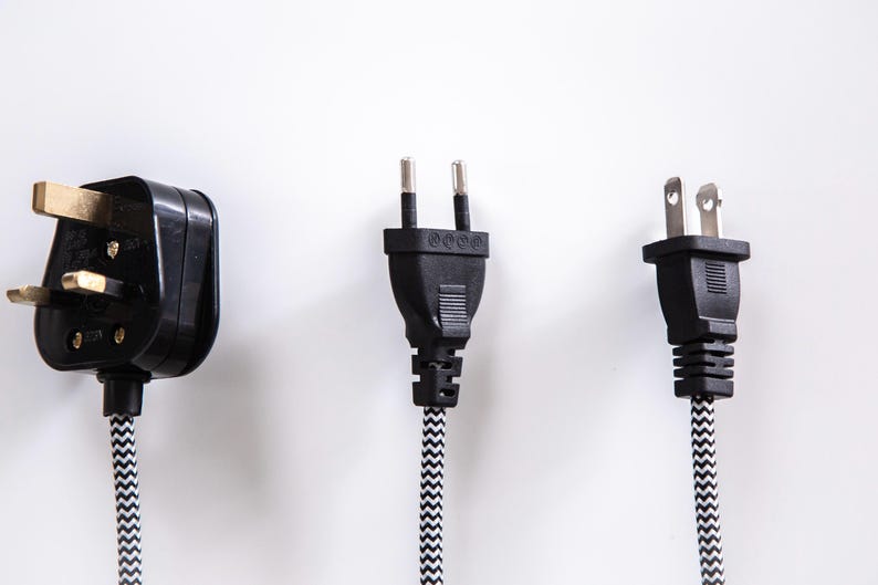 Pode incluir: Tr&ecirc;s tipos diferentes de tomadas el&eacute;tricas com cabos pretos e cabos com padr&otilde;es brancos e pretos. As tomadas est&atilde;o sobre um fundo branco.
